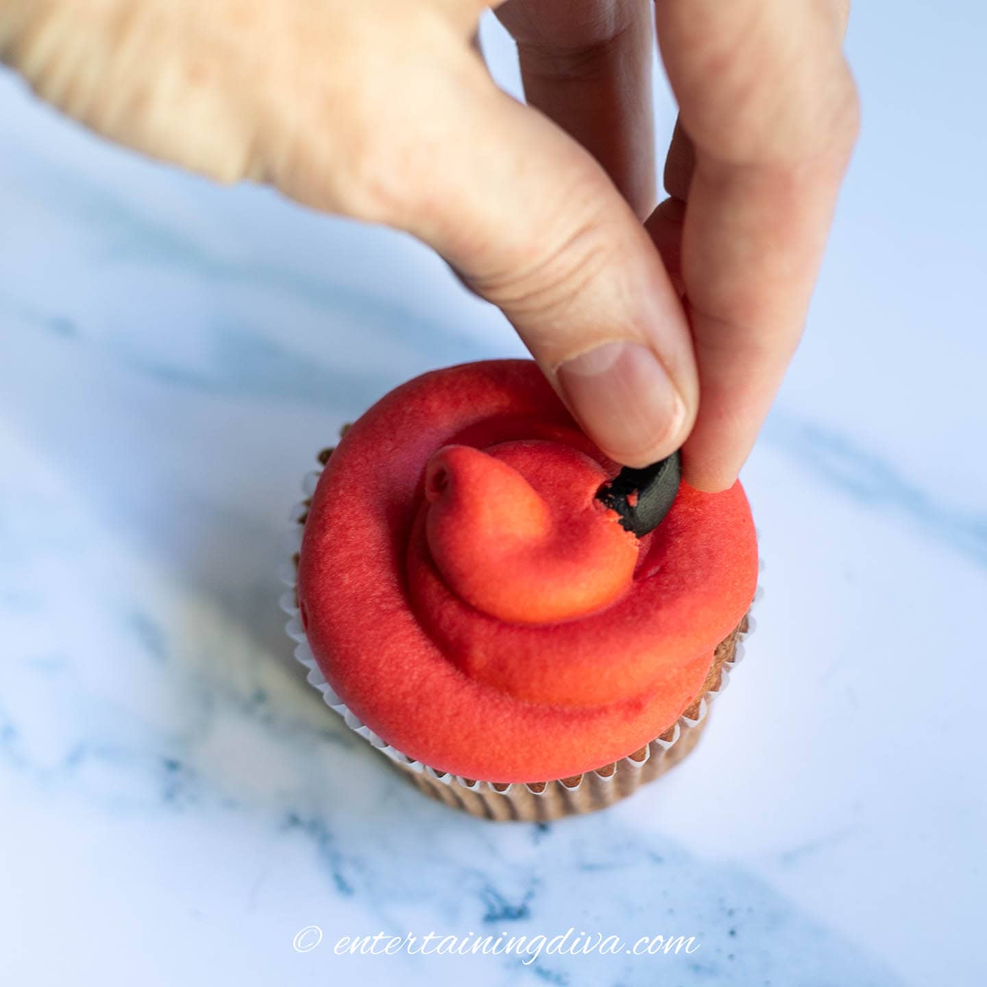 A fondant devil horn being pushed into the top of the cupcake icing