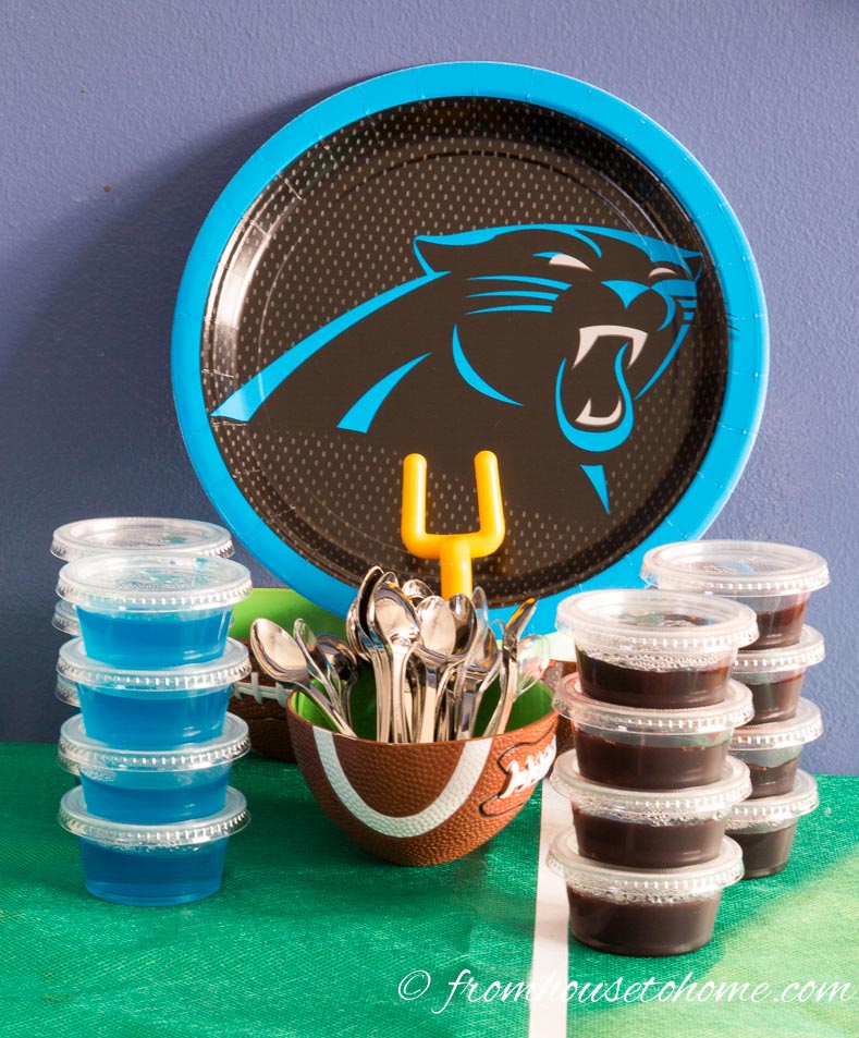 Blue and black jello shots stacked in front of a Carolina Panthers paper plate with a bowl of mini tasting spoons