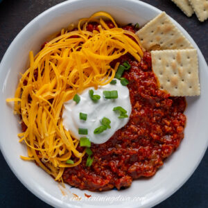overhead picture of crock pot no bean chili topped with sour cream, green onions, grated cheese and crackers