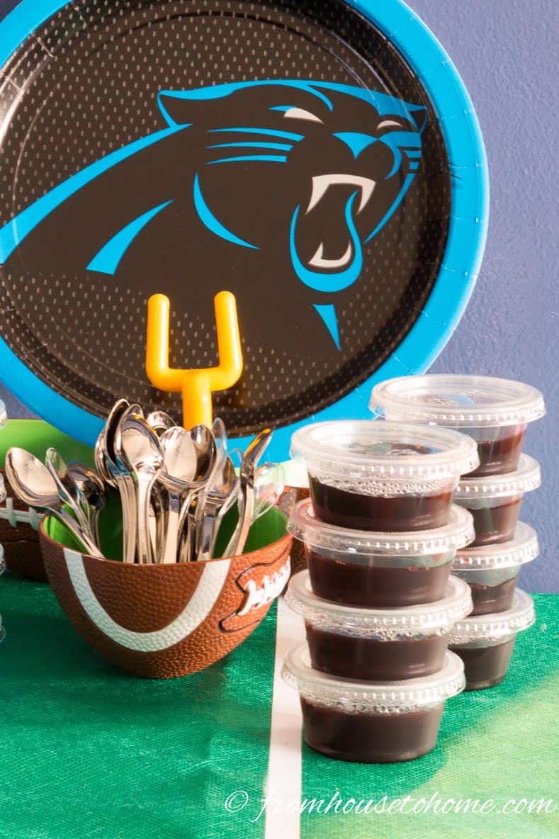 A stack of black jello shots beside a bowl filled with mini tasting spoons