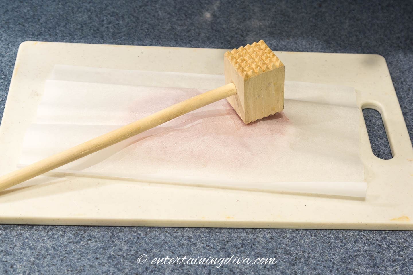 meat tenderizer on a parchment-covered chicken breast