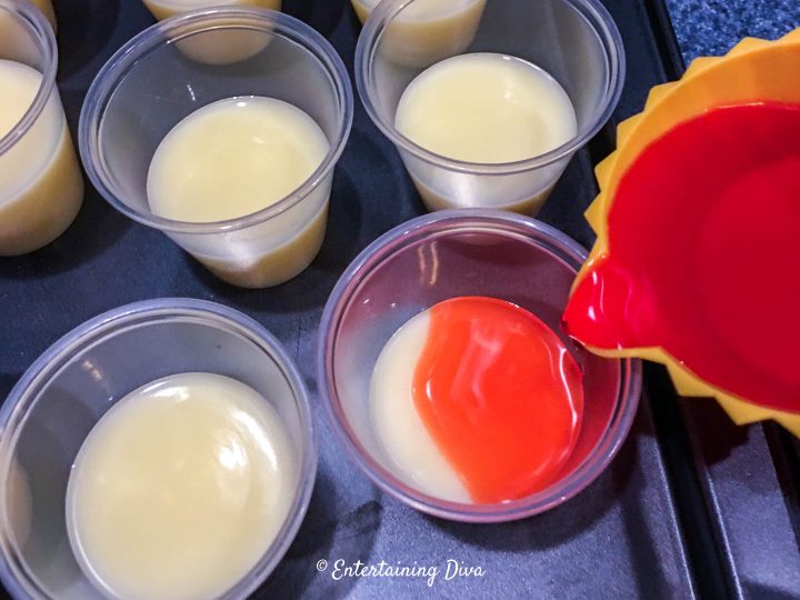 red jello being poured on top of the strawberry shortcake jello shot pudding layer