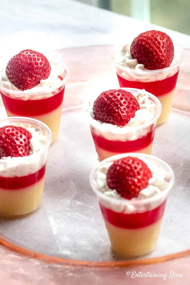 Red and white layered strawberry shortcake jello shots with whipped cream and strawberries