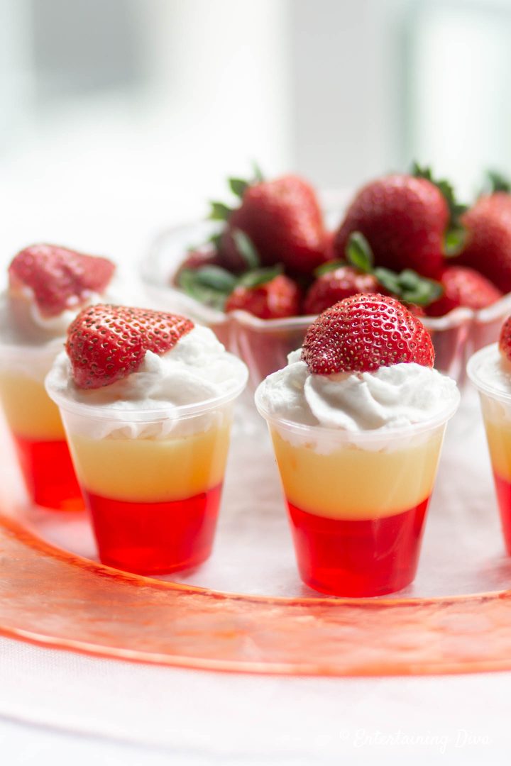Strawberries and cream layered jello shots recipe with strawberries in the background