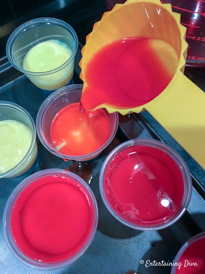 Red jello being poured onto the white pudding layer of the red, white and blue jello shots
