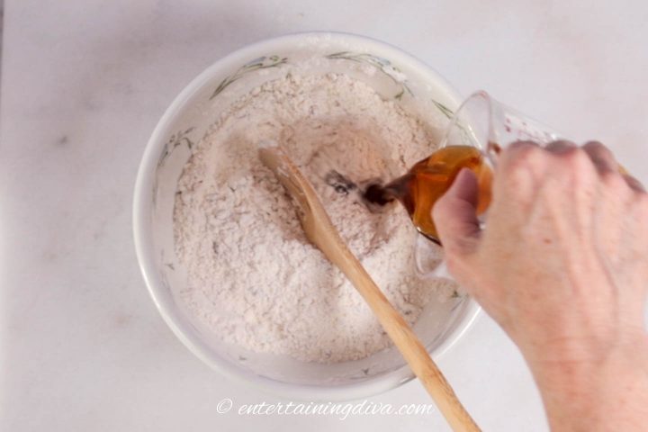 Maple syrup being added to the flour mixture in a bowl