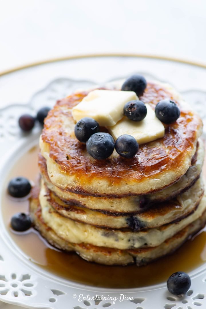 Blueberry buttermilk pancakes topped with blueberries, butter and maple syrup on a white plate