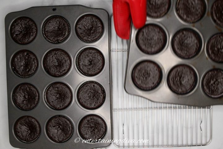 Muffin tins with chocolate cupcakes cooling on wire racks
