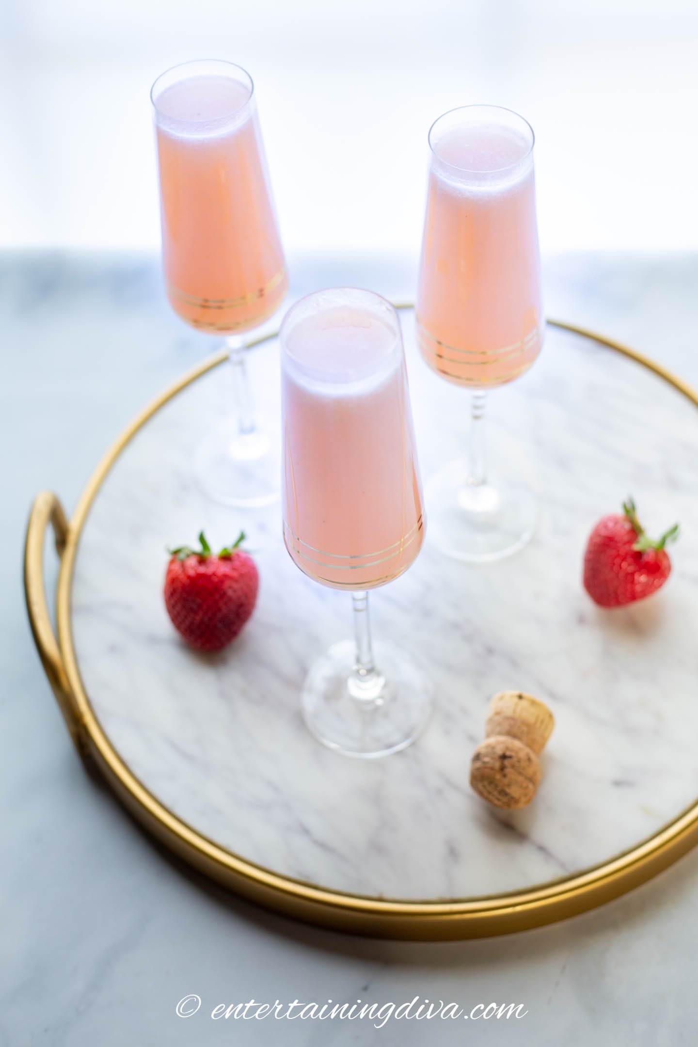 strawberry mimosas in champagne flutes on a marble tray