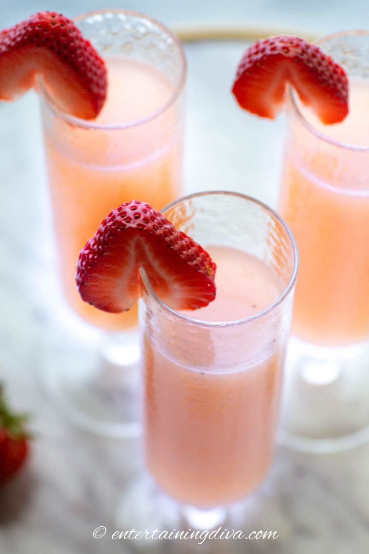 Close up of strawberry mimosas in champagne flutes with a sliced strawberry on the rim