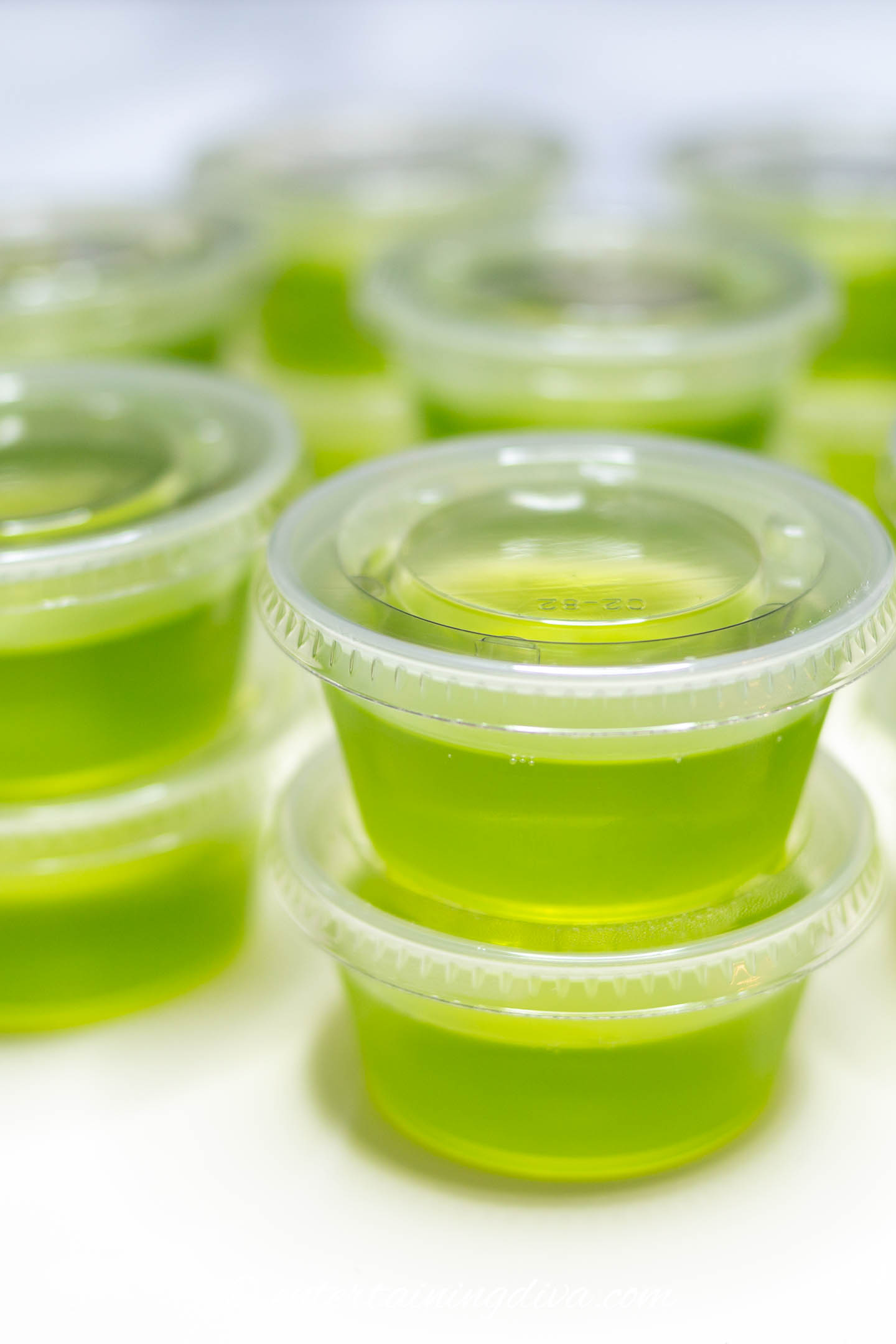 close up of green apple cinnamon fireball jelly shots in plastic shot cups with lids