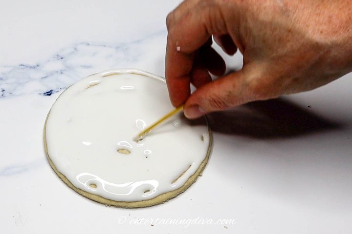 Toothpick fixing gaps in white royal icing on the moon cookie