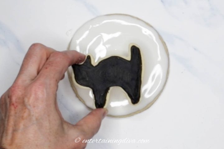 Black cat cookie being placed on the moon cookie