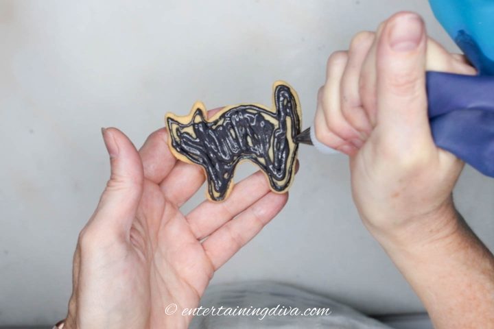 Black icing being flooded onto cat cookie