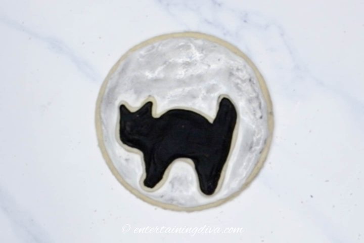 The silhouette cat cookie in front of a midnight moon cookie
