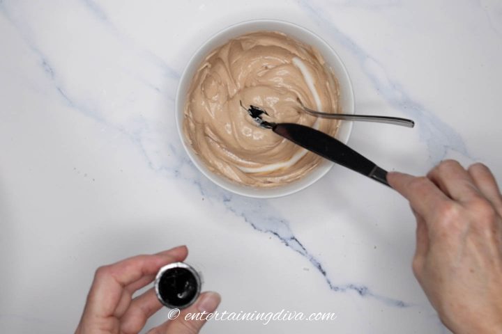 black food coloring being added to royal icing with cocoa powder
