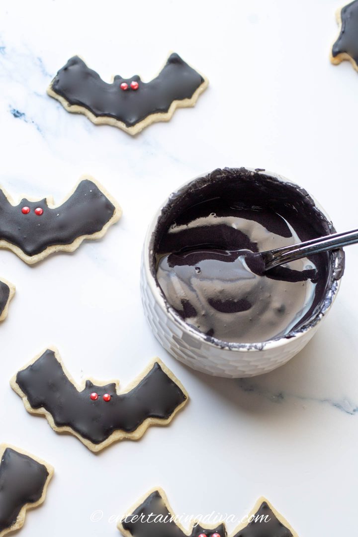 a bowl of black royal icing surrounded by bat cookies decorated with it