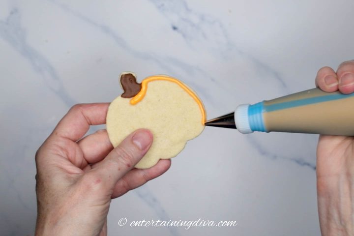 Decorated pumpkin cookie being outlined with orange royal icing