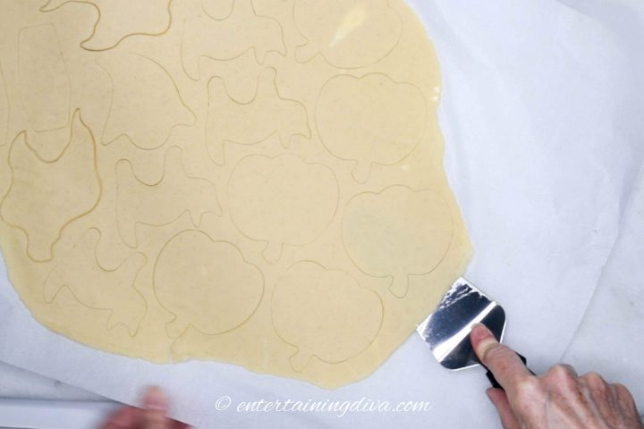 Pumpkin cut-outs being separated from parchment paper by a spatula
