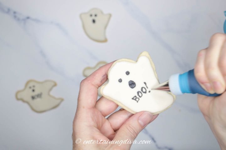 Boo! being piped on a ghost cookie with black royal icing