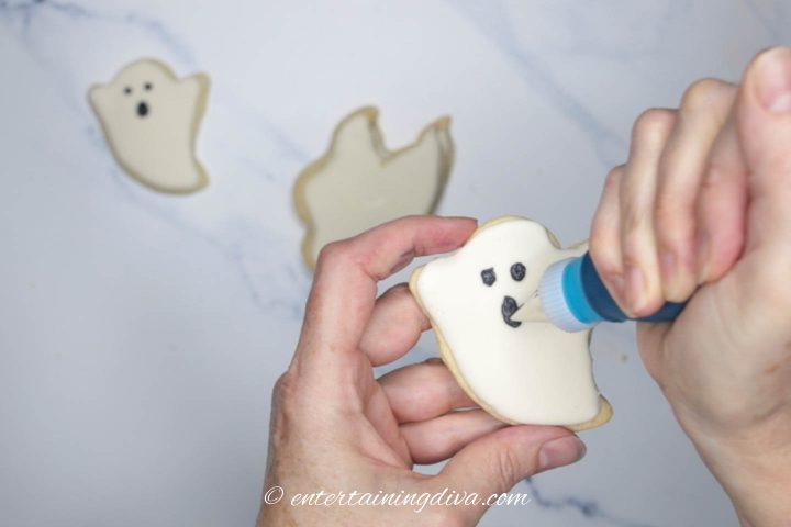 Black royal icing face being piped on a ghost cookie