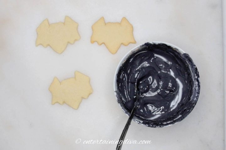 Plain Halloween bat sugar cookies beside a bowl of black royal icing