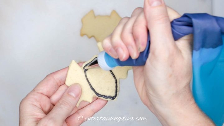 The middle section of larger bat sugar cookies being outlined with black royal icing