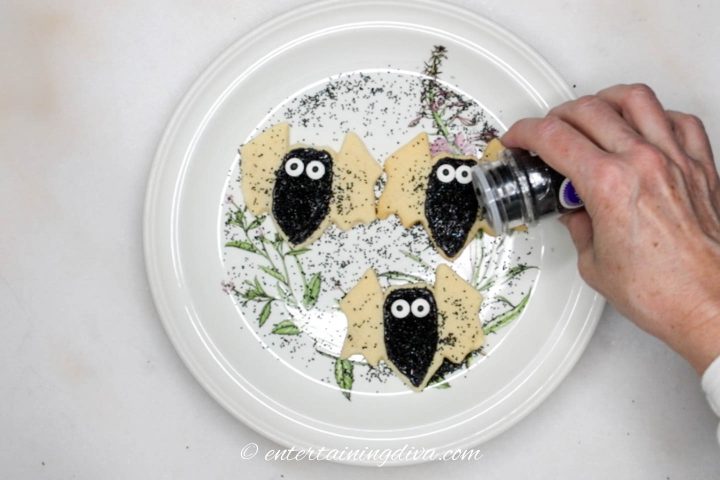 Black sprinkles being added on top the black icing on the bat cookies
