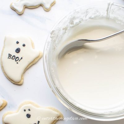 white royal icing in a bowl beside sugar cookies
