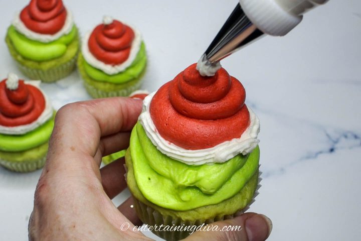 A white ball being piped onto the top of the Grinch cupcake Santa hat
