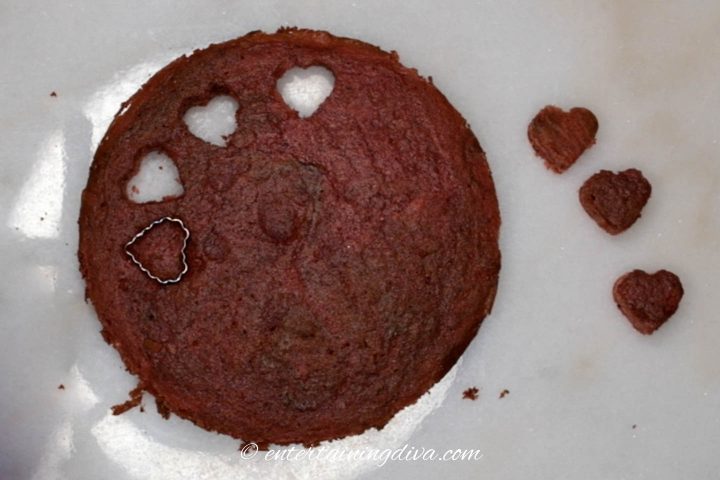 small hearts being cut out of a red velvet cake layer