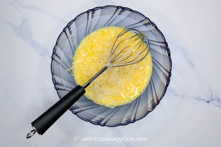 Egg and grated cheese mixture in bowl with whisk