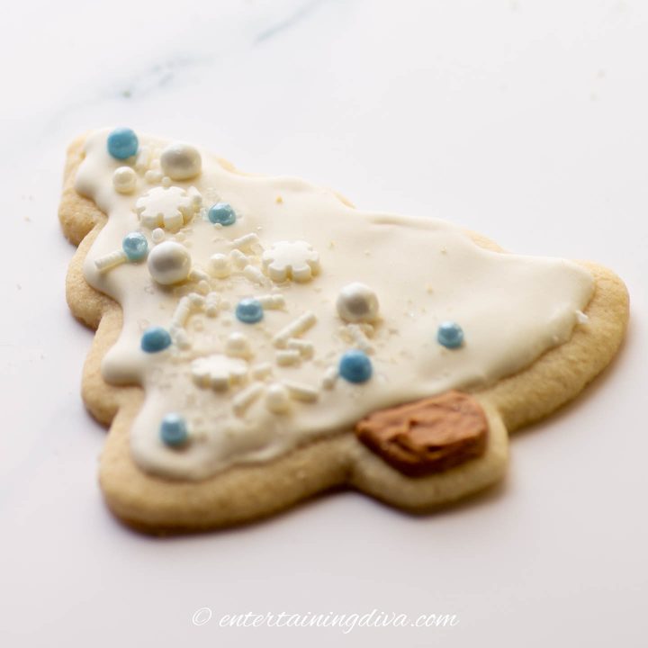 Christmas tree sugar cookie decorated with white royal icing and blue and white sprinkles
