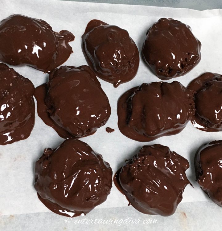 Homemade turtles covered in melted chocolate on a cookie sheet