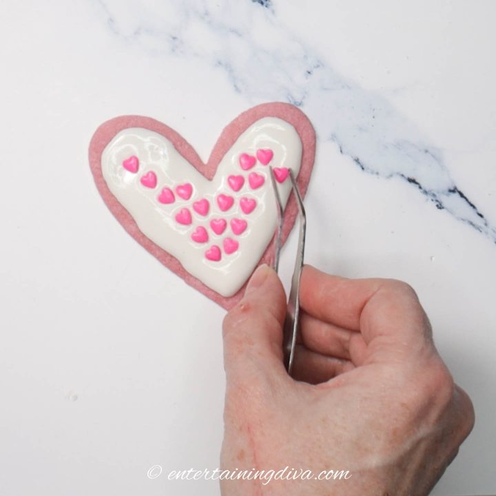 Heart cookie decorated with white royal icing and pink heart sprinkles