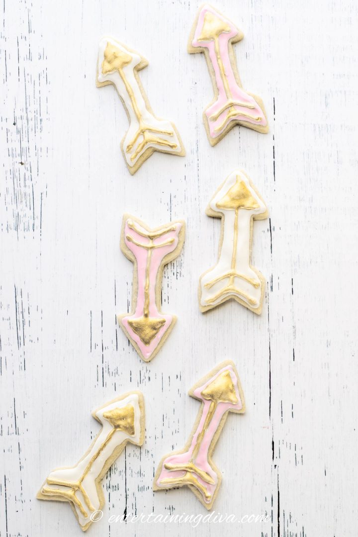 Arrow cookies decorated with white and pink royal icing and gold edible paint