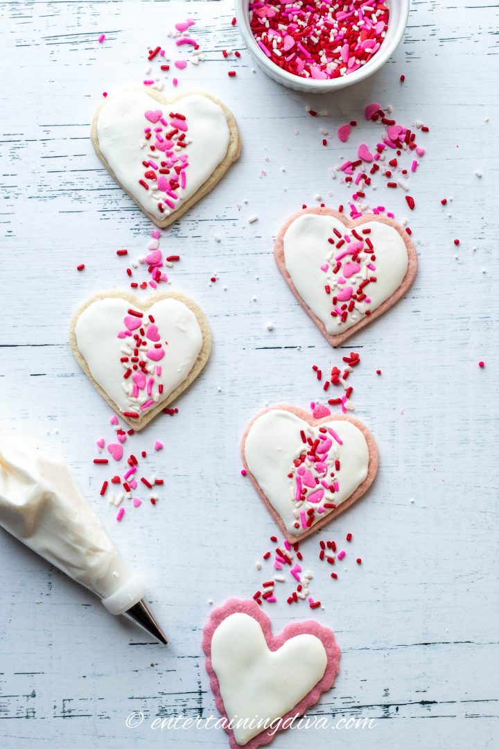 Heart cookies decorated with white icing and pink, white and red sprinkles in a band down the middle