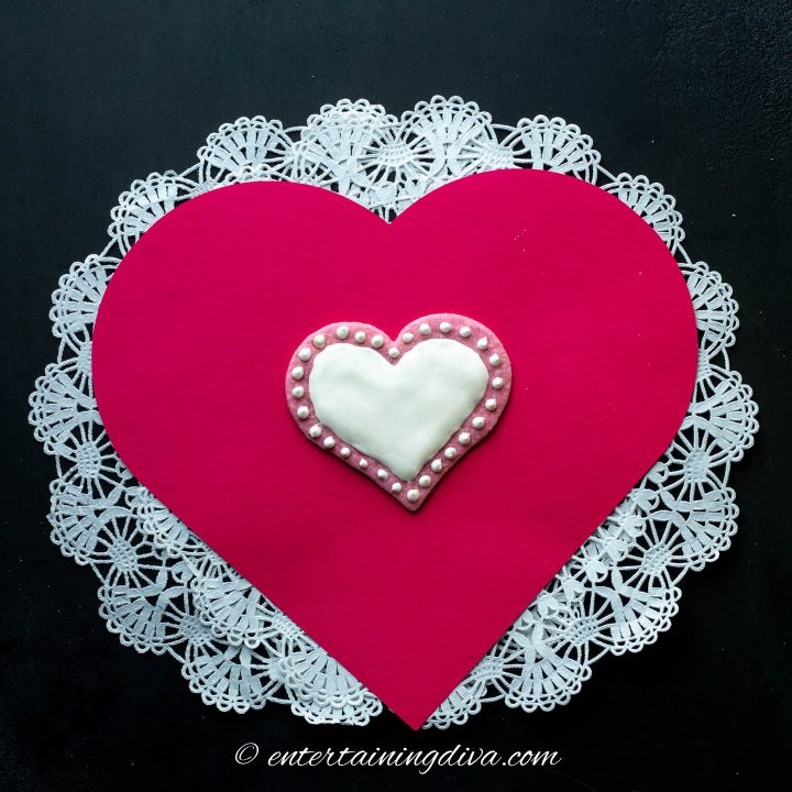 Pink heart cookie decorated with white royal icing edged in white icing dots
