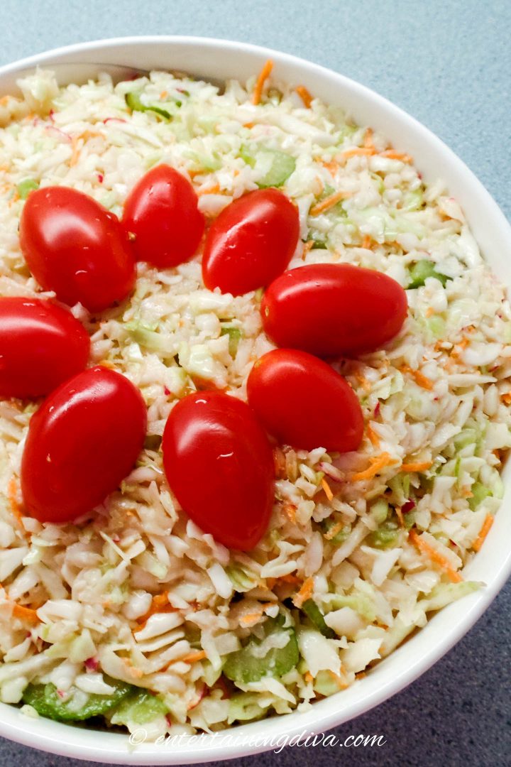 top view of coleslaw garnished with cherry tomatoes in a white bowl