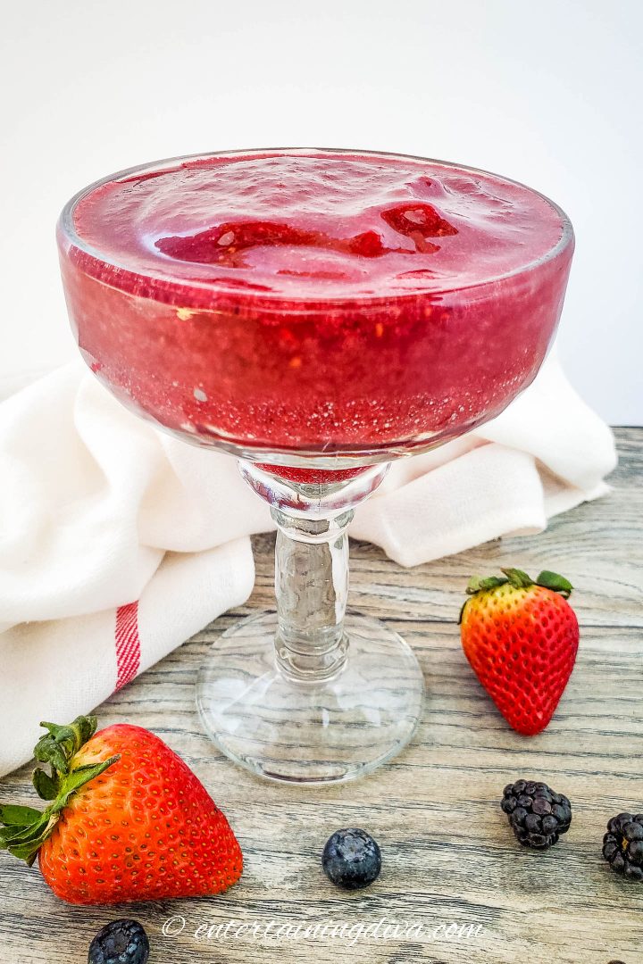 mixed berry frozen margarita in a glass with strawberries, blackberries and blueberries surrounding it