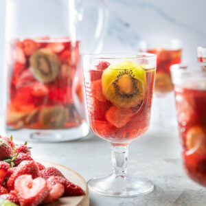 strawberry kiwi sangria in a glass with a pitcher behind