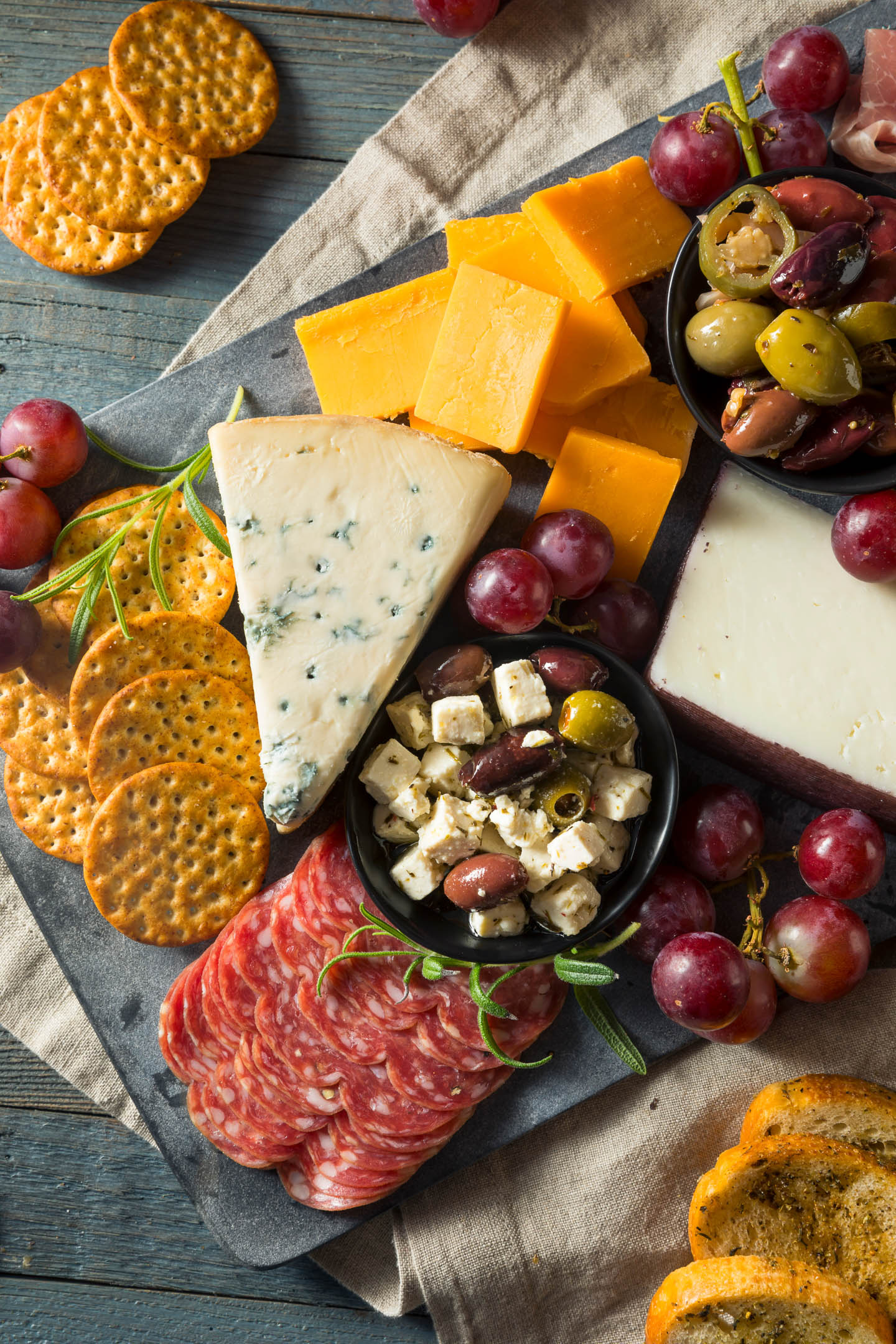 Rectangular charcuterie board with cheeses, olives, grapes, slices of meat and bread