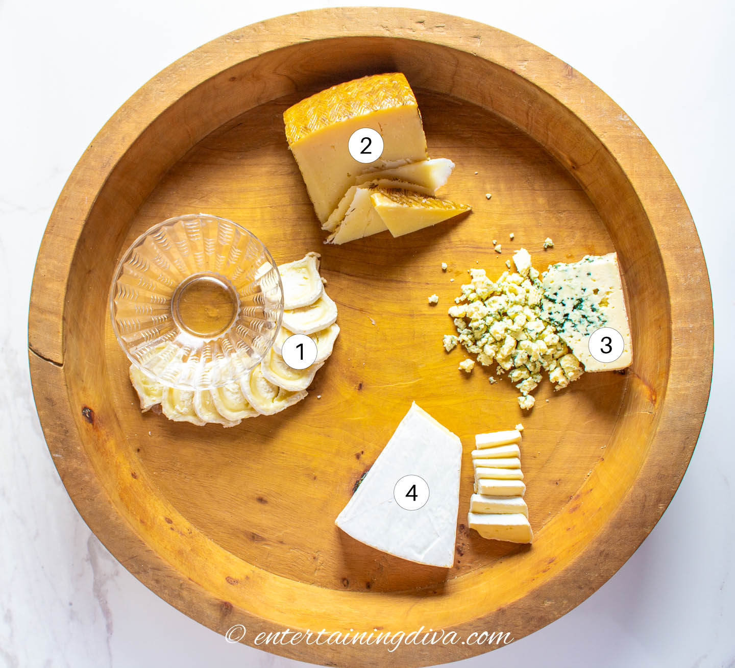 A round charcuterie board with goat cheese, Parmesan, gorgonzola and brie arranged on it