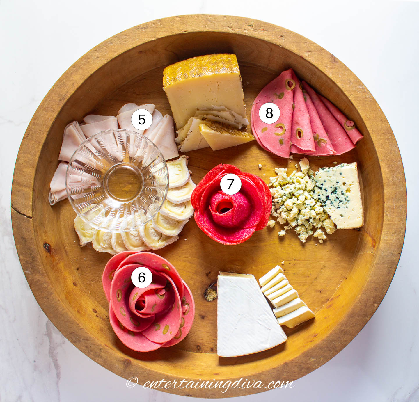 A round charcuterie board with 4 cheeses and ham, salami and mortadella arranged on it