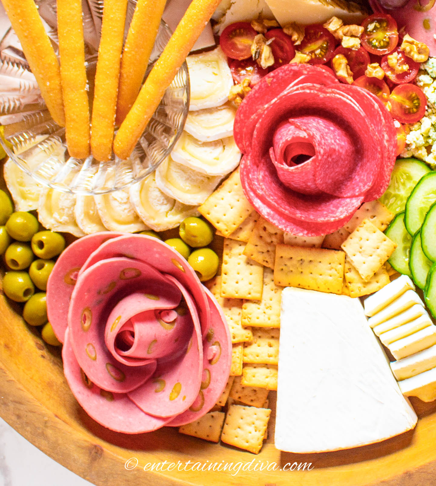 Meats made into flowers on a charcuterie board with crackers, olives and cheeses