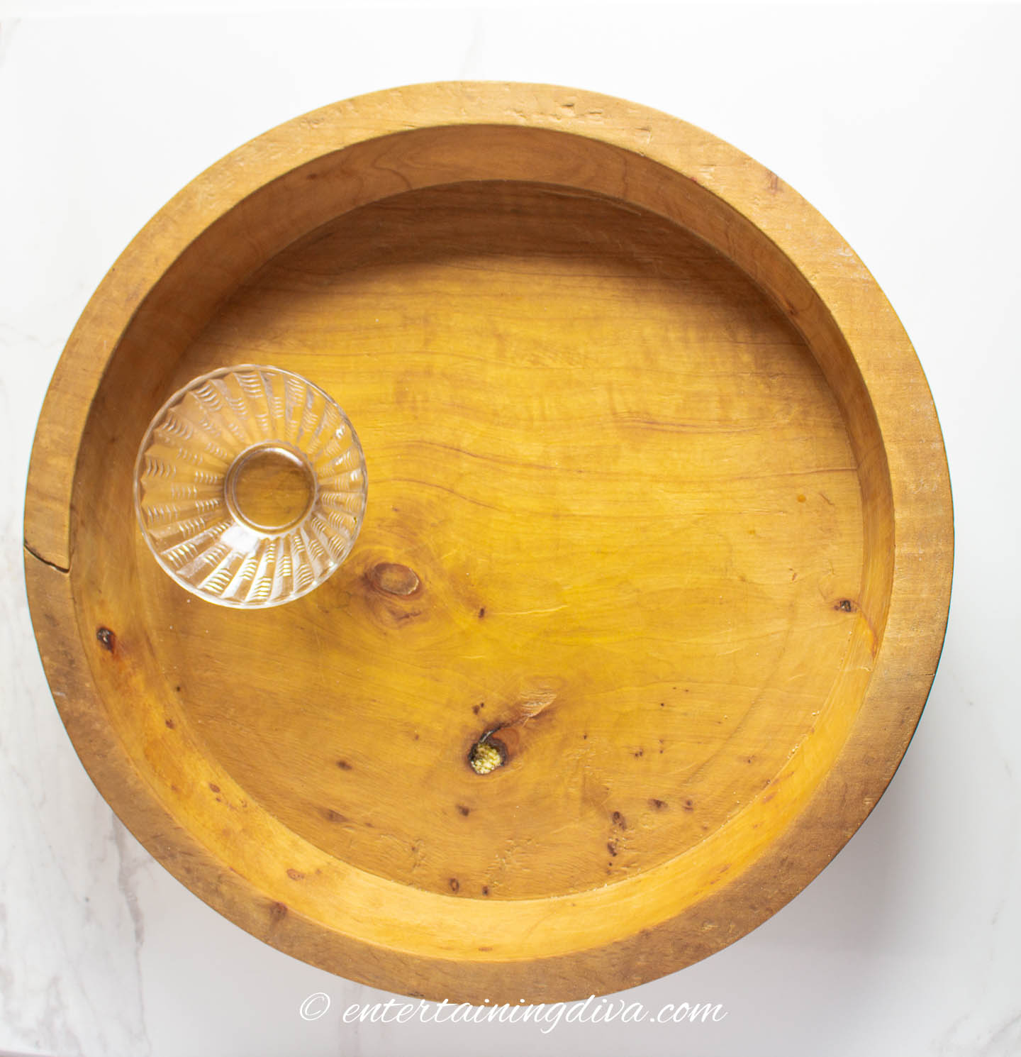 A wooden pie plate used as a charcuterie board with a small bowl on it