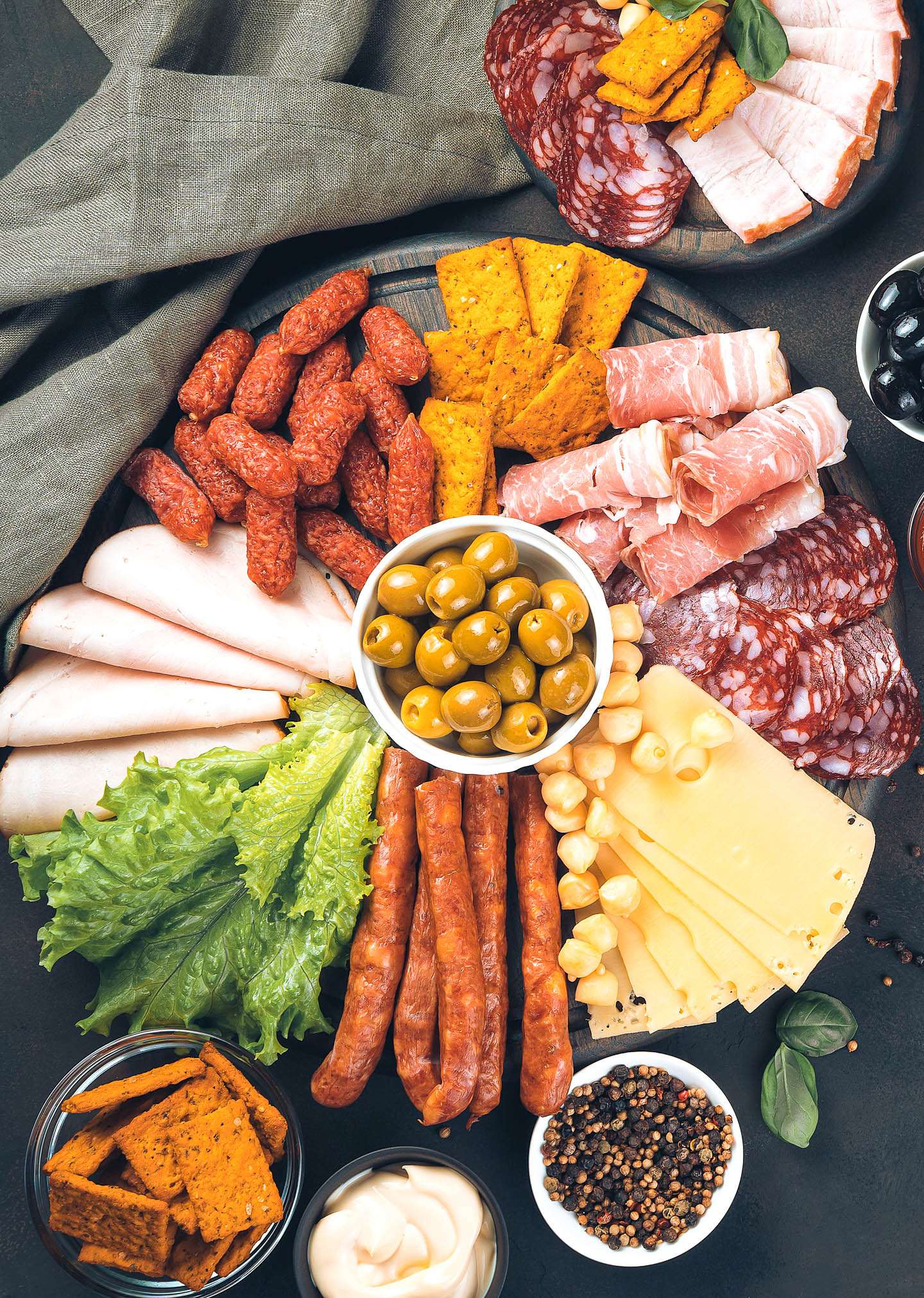 A round charcuterie board with a bowl of olives in the middle and various meats, cheeses and crackers spread out on the board