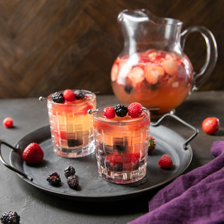 two glasses of triple berry rose sangria on a tray with a pitcher in the background
