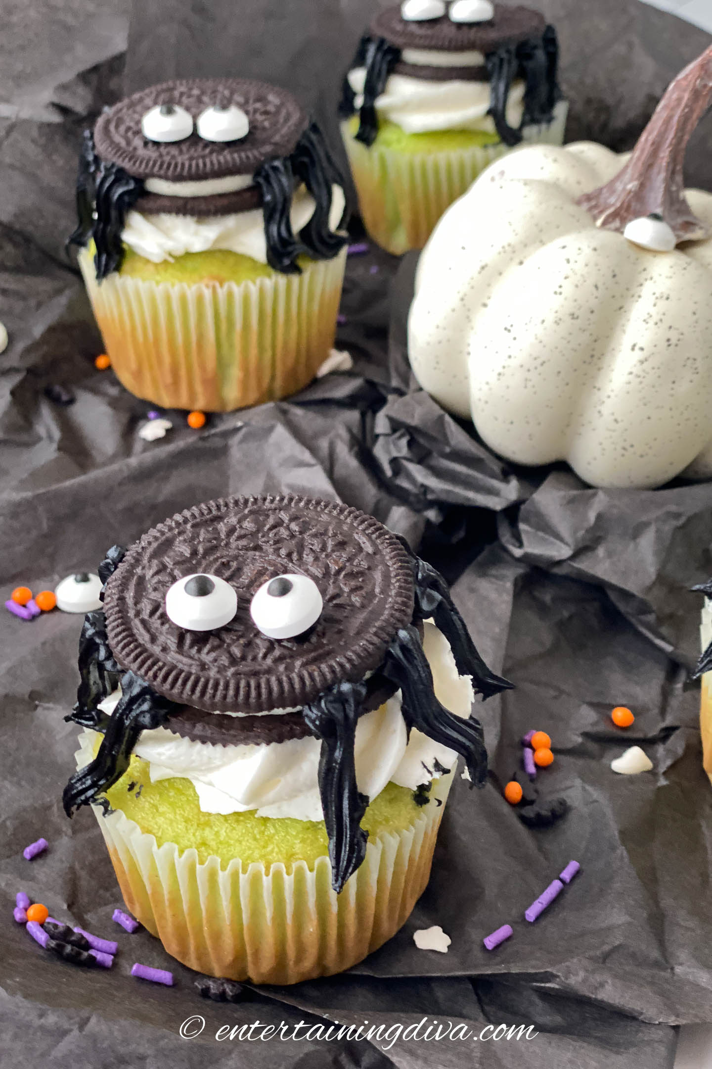 Halloween Oreo spider cupcakes with a white pumpkin and sprinkles on a black surface