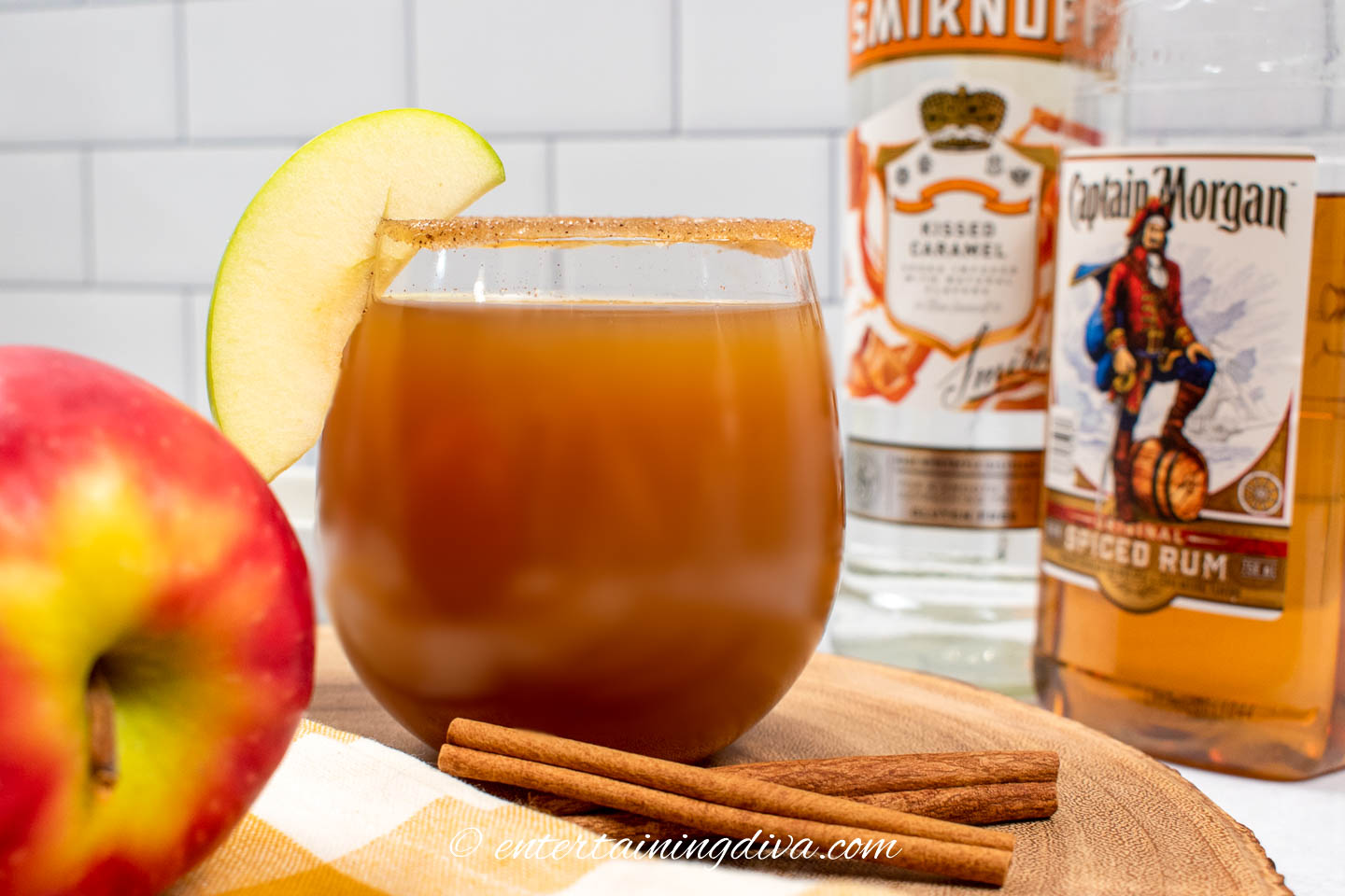 spiked caramel apple cider in a glass with spiced rum and caramel vodka bottles in the background
